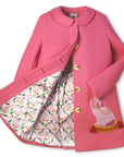 Pink merino wool A-line coat with embroidered dogs, gold buttons, and satin lattice print lining. Features hidden placket and back pleat detail.