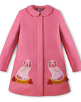 Pink merino wool A-line coat with two embroidered dog motifs on tufted pillows, hidden placket, and a Peter Pan collar