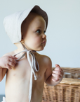 Baby in a wheat-colored linen sun bonnet with a wide brim and chin ties, shown from the side