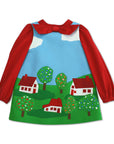 Flat-lay of the Little Cloud Dress with a red bow blouse, featuring appliqued houses and embroidered trees.