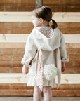 Child wearing a cream-colored bunny coat with a hood, long ears, and a fluffy tail, designed by Little Goodall.