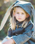 Close-up of a young girl outdoors wearing the Flopsy Bunny Coat, a handcrafted wool coat with bunny ears and toggle closures,