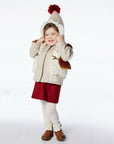 Smiling toddler wearing the Little Goodall Lucky Llama Coat, a wool winter jacket with faux fur llamas, red accents, and a pointed hood with a pompom