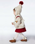 girl wearing the Little Goodall Lucky Llama Coat, a merino wool jacket with faux fur lining, embroidered llamas, and a pointed hood with a red tassel