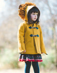 Child wearing Little Goodall Luxe Lion Coat in gold wool, standing outdoors with lion hood up. Cozy and stylish duffle jacket for fall and winter