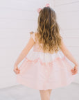 Back view of Little Goodall Pink Gingham Bunny Love Dress, featuring button details, ruffled trim, and gingham straps with bunny ear accents.
