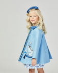 Girl in a light blue wool coat with embroidered dog, tasseled pillow, and button details, shown from the side.