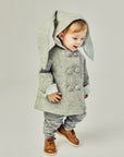 Boy wearing grey bunny coat with cuffed sleeves and hood up. One ear shows the grey exterior, the other reveals the light blue lining. Cozy and stylish