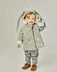 Smiling boy wearing grey bunny coat with hood up, revealing plush lining. One ear flops down while the other is lifted. Double-breasted buttons