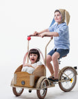 Two children on a tricycle, with one wearing a grey bunny hat featuring floppy ears