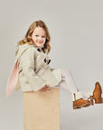 girl wearing the Little Goodall Snowshoe Rabbit Coat – a merino wool jacket with bunny ear hood, toggle fasteners, and plush faux fur lining for kids