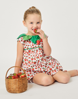 Toddler girl wearing a strawberry-print romper with a green leaf collar, sitting with a basket of strawberries
