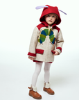 young girl wearing a Hungry Caterpillar wool coat with the hood up, featuring playful caterpillar details, red accents, and matching tights and boots