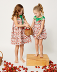 Toddler and girl in coordinated strawberry dresses and rompers, sharing a basket of strawberries