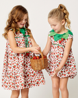 Toddler and girl in coordinated strawberry dresses and rompers, sharing a basket of strawberries
