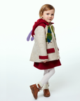 Young girl in a Hungry Caterpillar wool coat with red accents and antennae hood, paired with a red dress and boots, shown from a side view