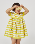 Smiling child in a lemon print dress holding lemon slices over her eyes, wearing The Very Hungry Caterpillar Lemonade Dress