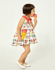 Girl in cotton Two Scoops Dress with ice cream pockets and coral collar, licking an ice cream cone. Playful candy-themed summer outfit for kids.