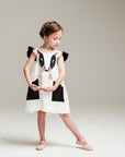 Girl wearing a white cow dress with black appliqué details, flutter sleeves, and a 3D cow face design. Whimsical farm animal outfit.