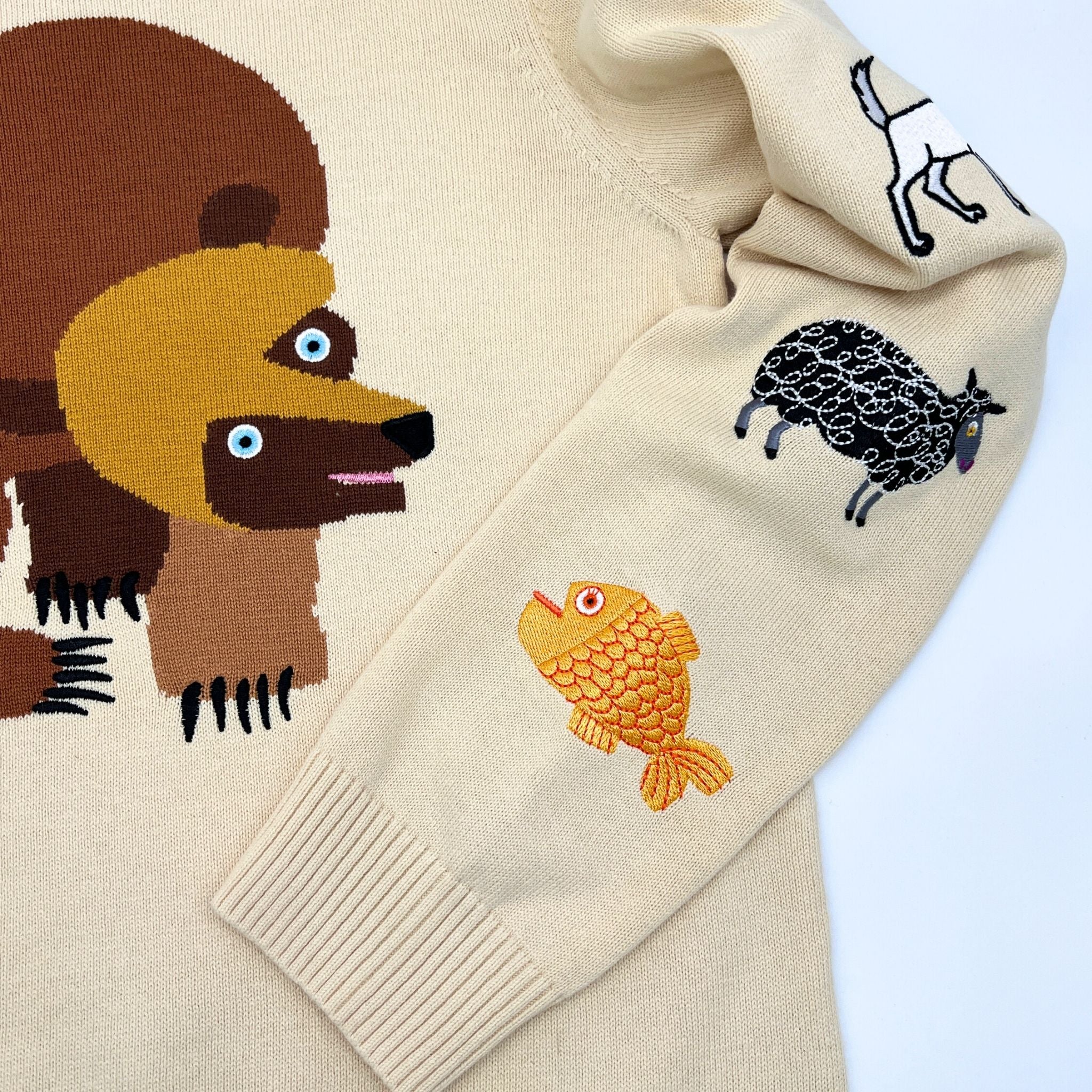 Beige sweater with bear on front and embroidered fish and sheep designs on the sleeve