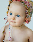 Baby wearing floral bonnet, with tassles tied as a bow.