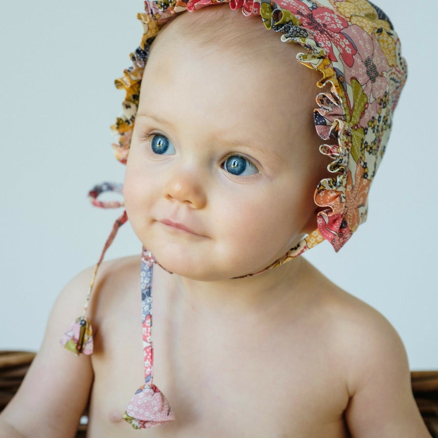 Baby wearing floral bonnet, with tassles tied as a bow.