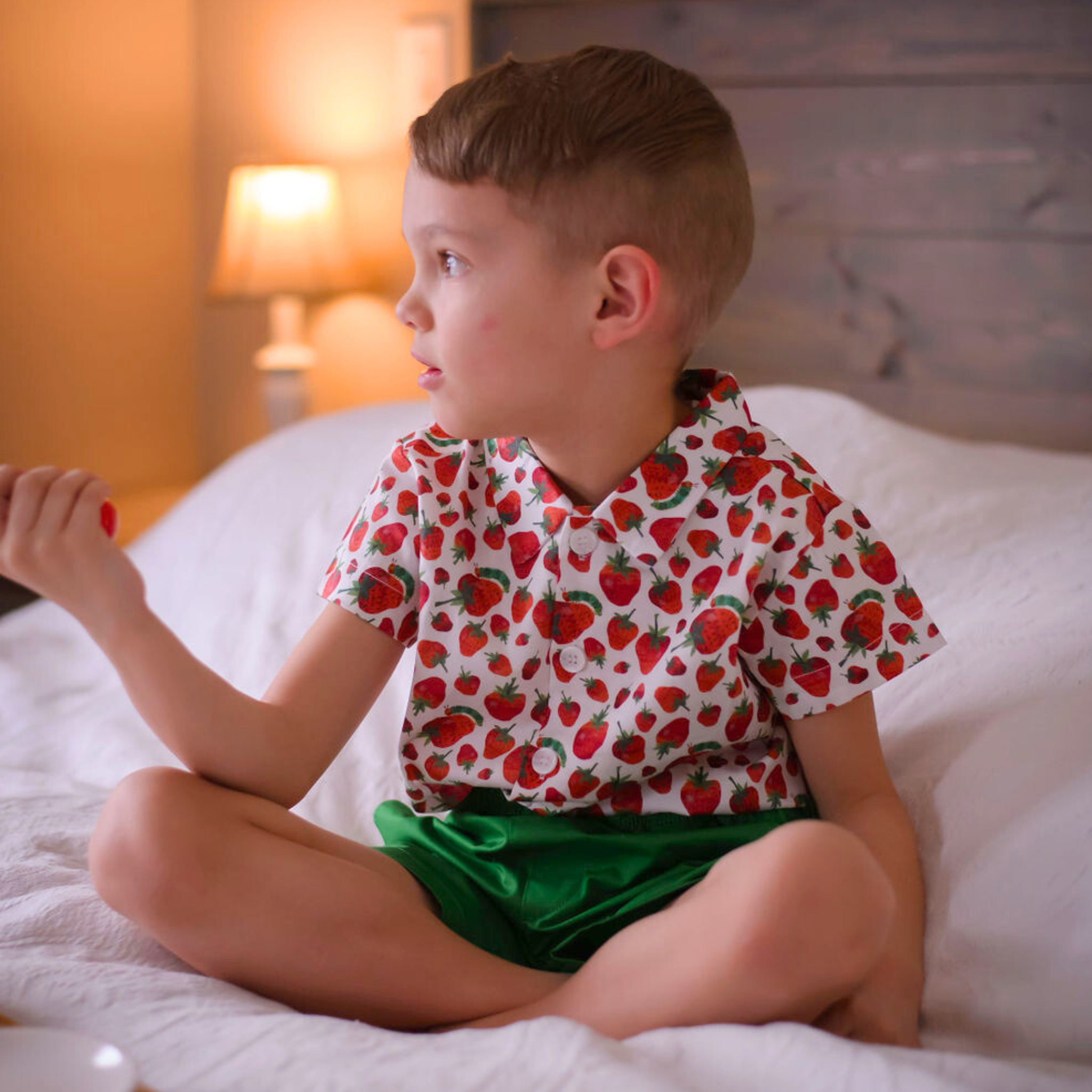 Child wearing a strawberry print short-sleeve button-up shirt and green shorts, part of The Very Hungry Caterpillar collection