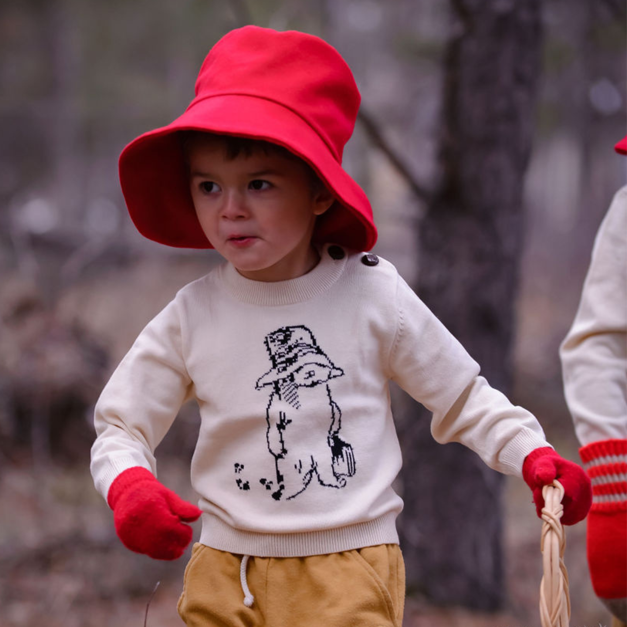 a child dressed in a cozy Paddington Bear sweater and red bucket hat