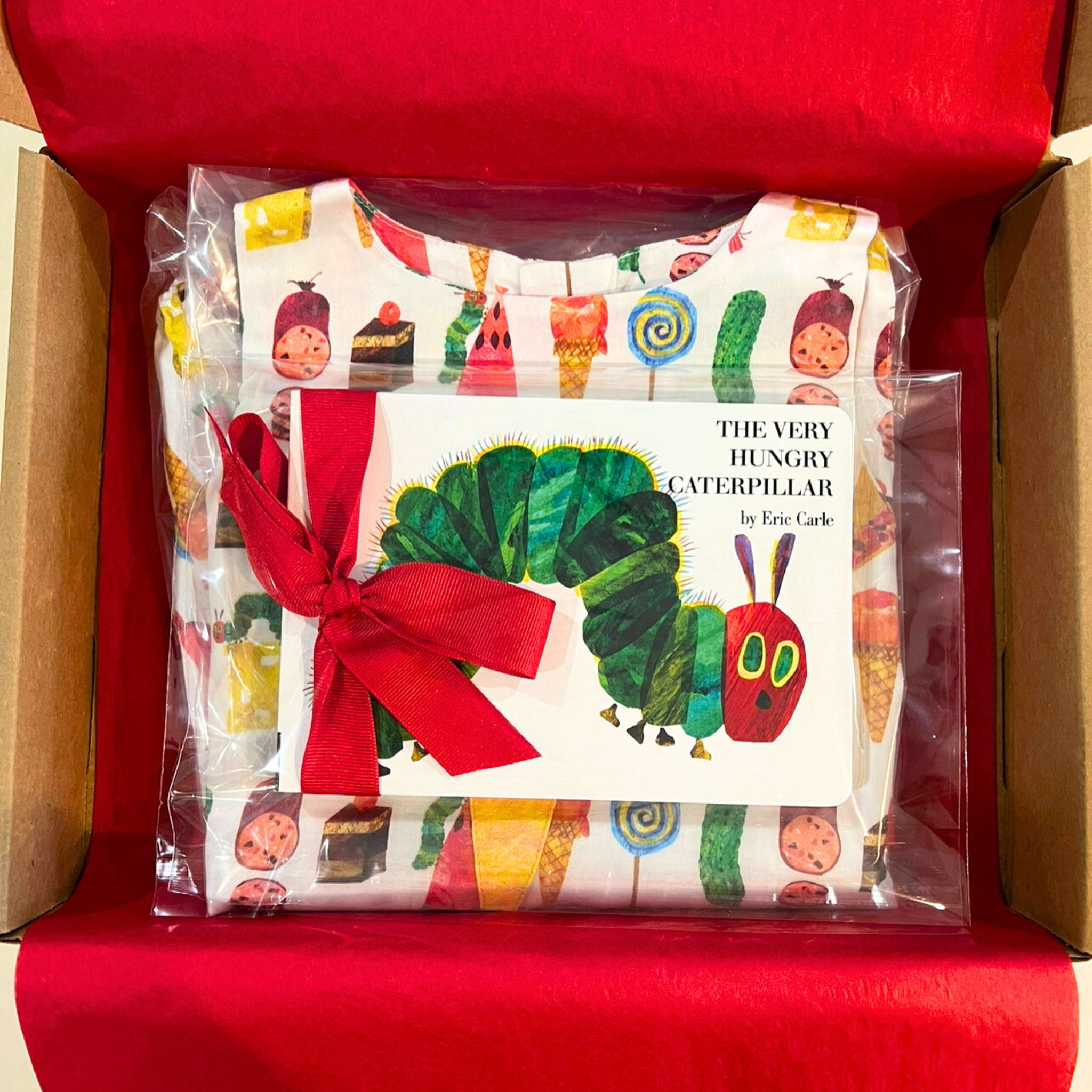 Hungry Caterpillar romper and board book gift set, packaged with a red ribbon. Features a 100% cotton romper for kids with colorful food prints