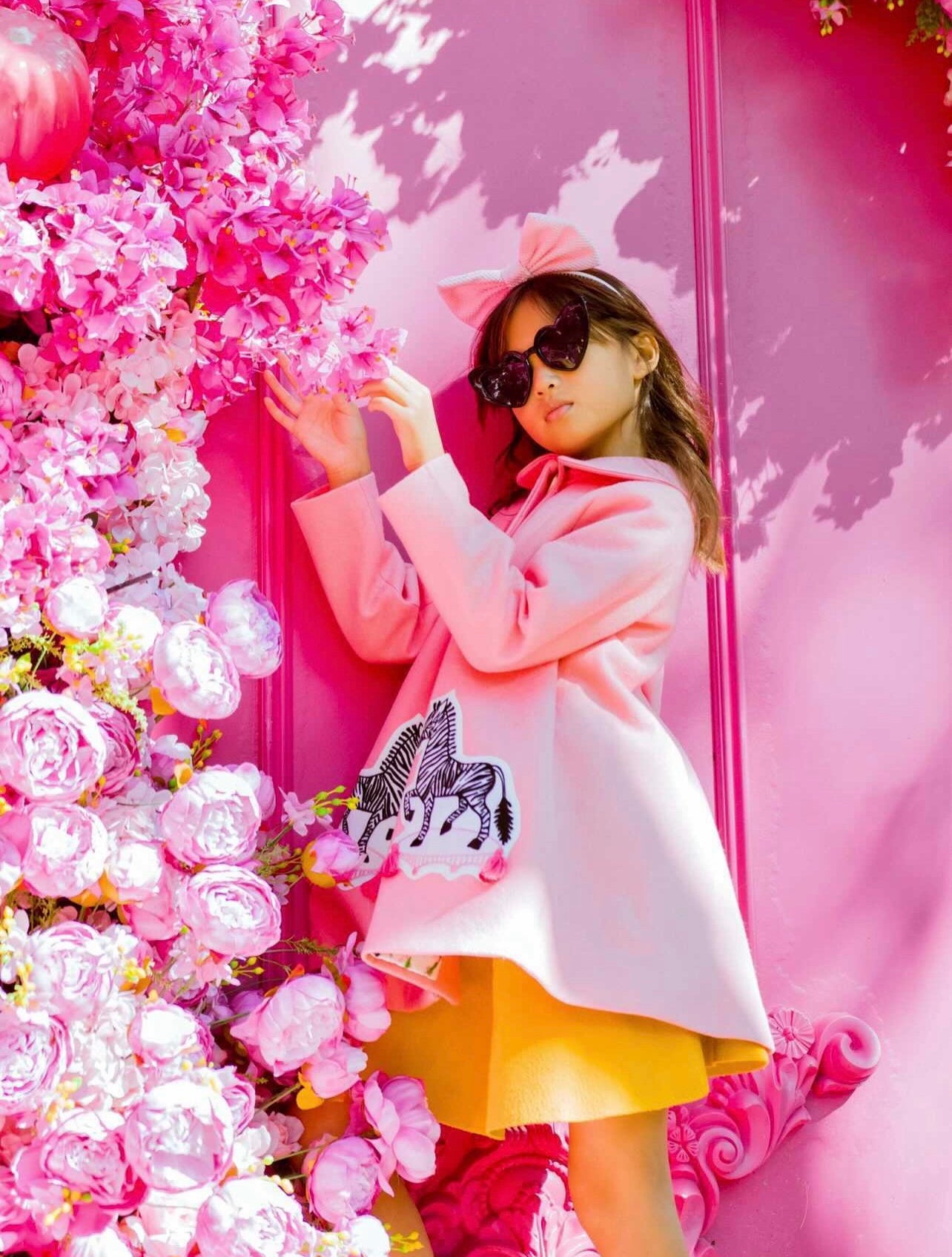 Fashionable child in a pink wool coat with zebra appliqué, standing near a pink floral backdrop