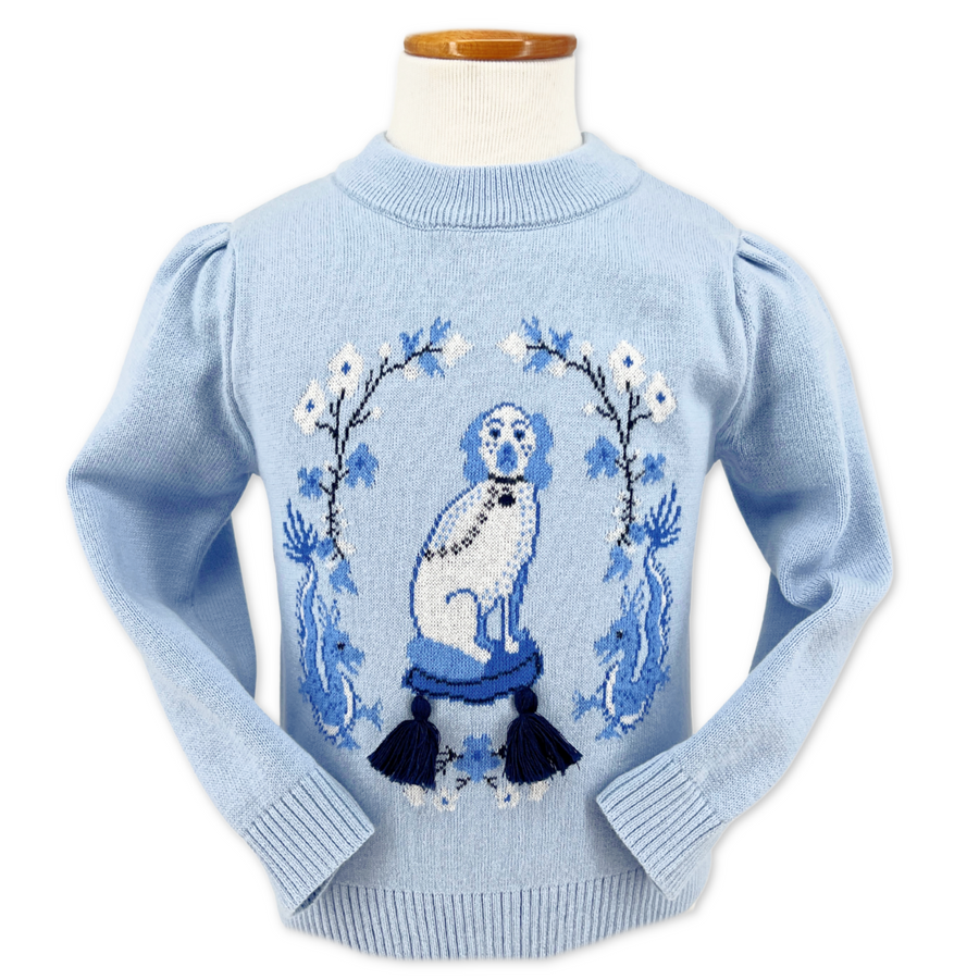 Light blue sweater with puffed shoulders and ribbed edges, featuring a dog on a blue tasseled cushion framed by floral patterns