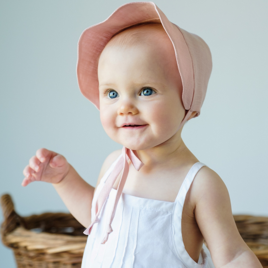 Baby wearing a pink linen scallop bonnet with a sun brim, fully lined for comfort.