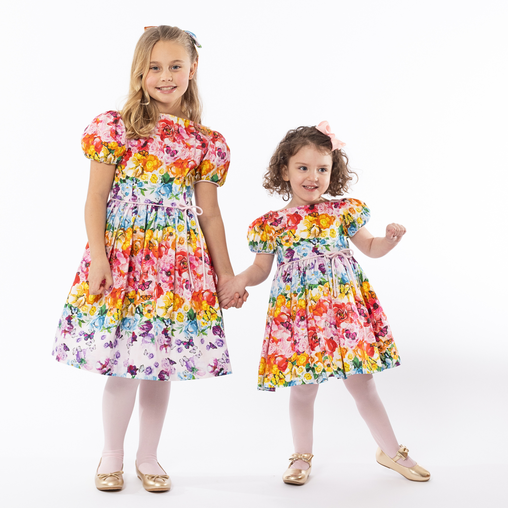 Two girls in matching Rainbow Bloom Party Dresses with puff sleeves and floral butterfly prints, perfect for special occasions and family portraits