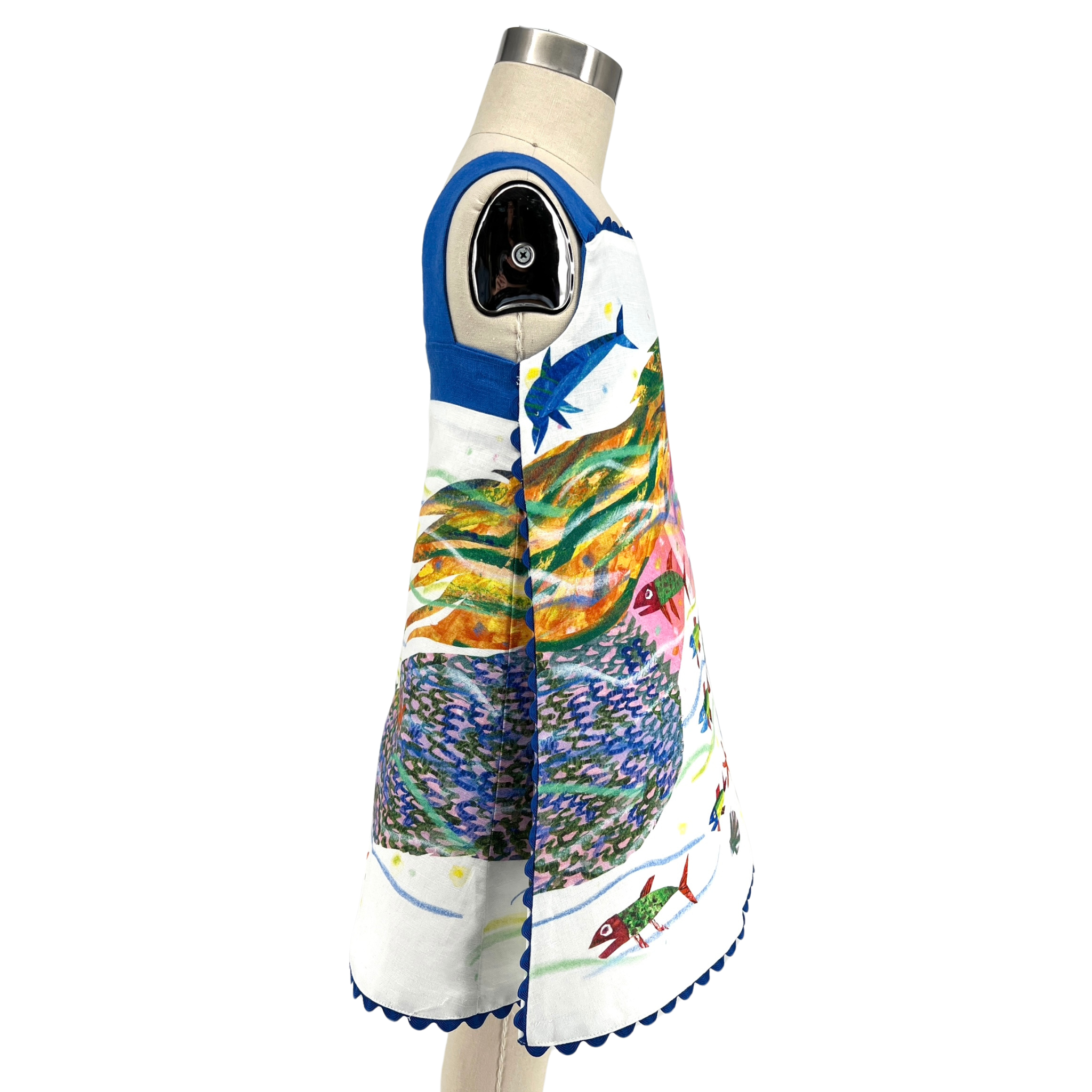 Side view of a sleeveless mermaid dress with fish swimming among coral and seaweed, finished with ocean-blue scalloped trim