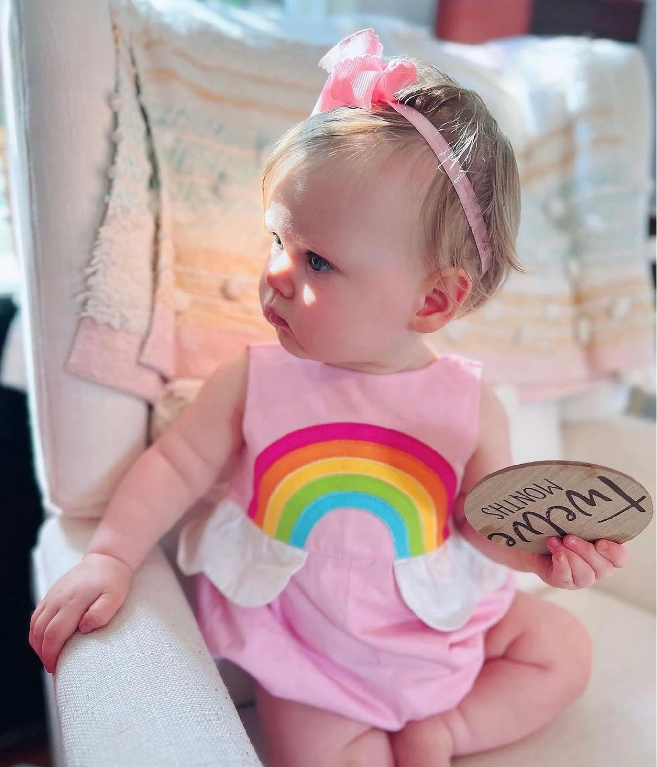 Baby girl wearing Over the Rainbow Bubble Romper in Sunset Pink with a rainbow applique and cloud peplum, a charming summer outfit
