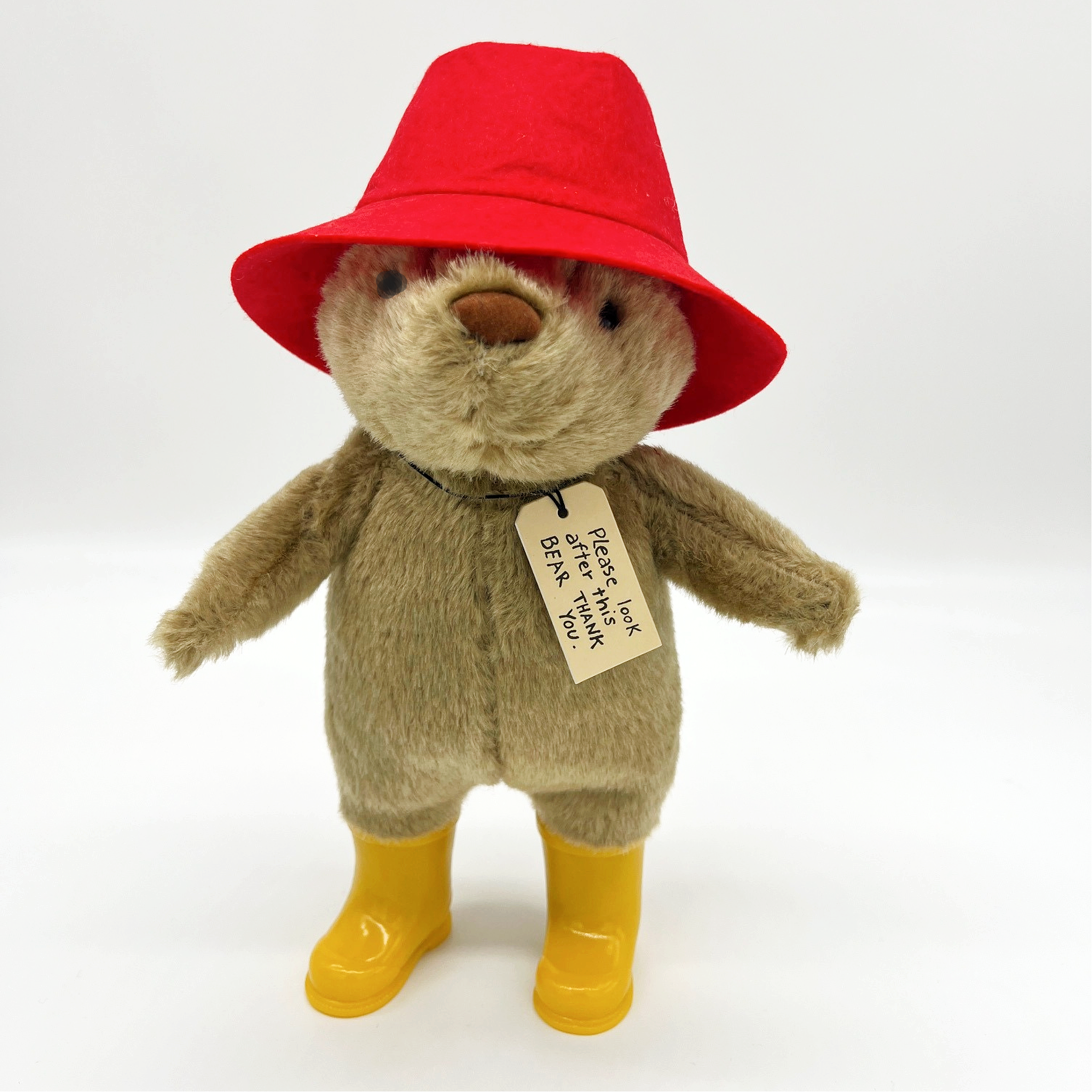 Paddington Bear 10" plush toy with red hat, yellow boots, and "Please Look After This Bear" tag, perfect for collectors and kids ages 3+