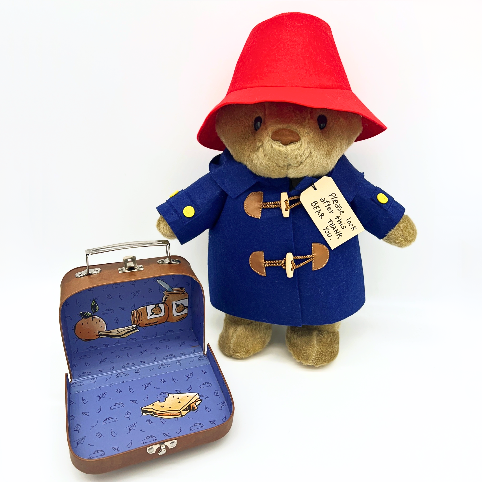 16-inch Paddington Bear plush toy in a red hat and blue wool duffle coat, next to an open illustrated suitcase with marmalade sandwich details
