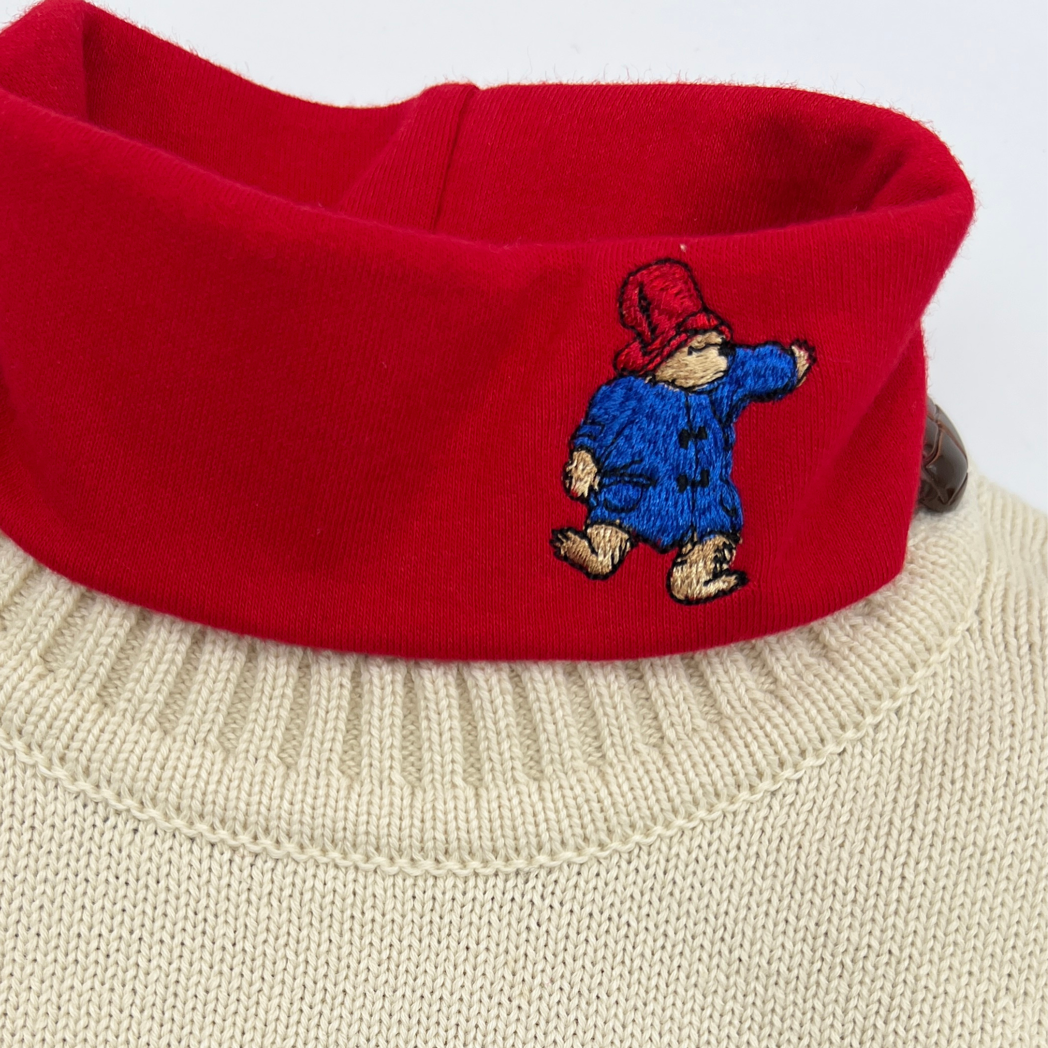 Little Goodall organic cotton red turtleneck for kids featuring an embroidered Paddington Bear on the collar. Soft, cozy, sensory-friendly, and perfect for layering