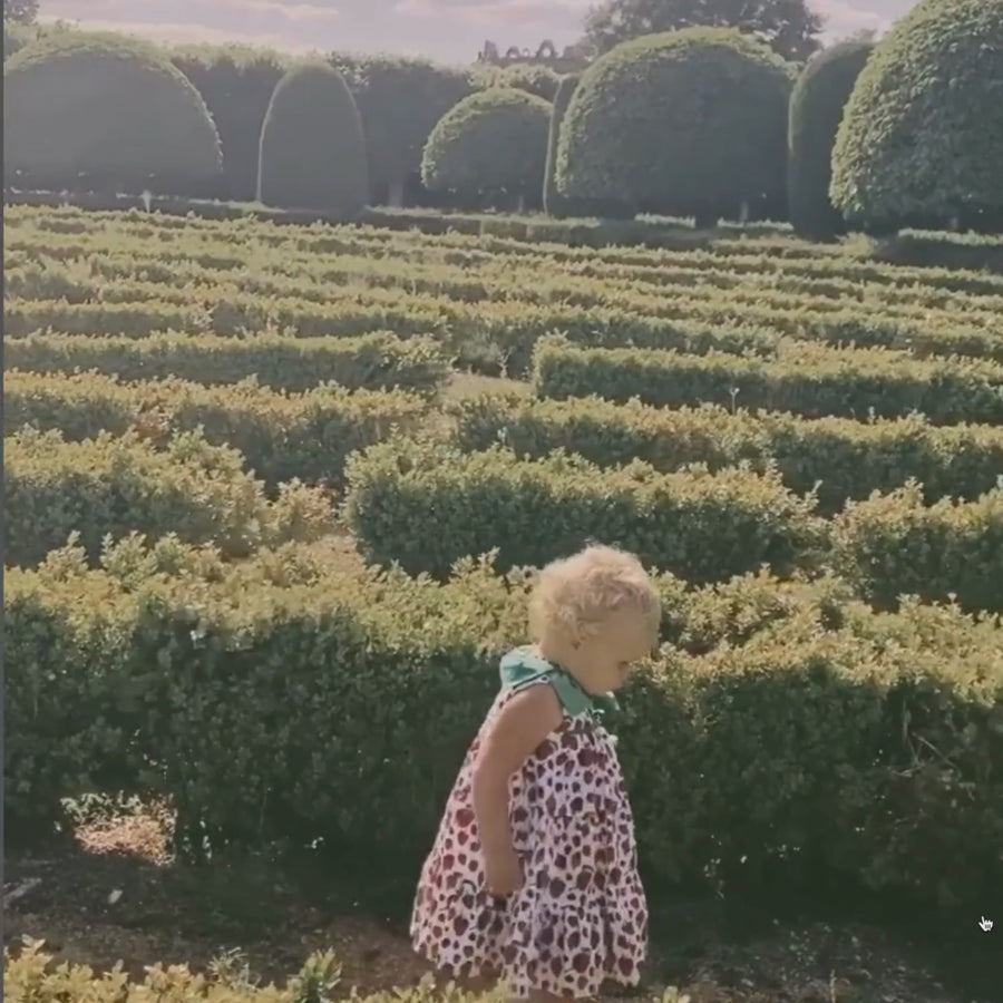 video showcasing A young girl walking gracefully in a strawberry-print dress with a green leaf colla