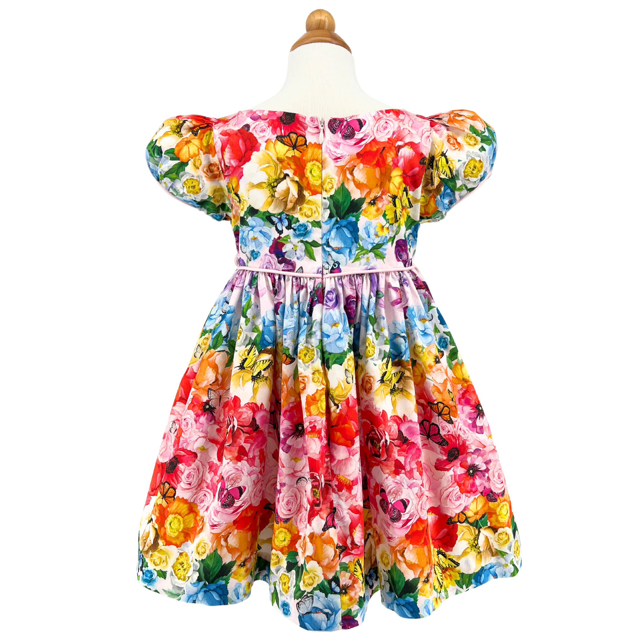 Back view of the Rainbow Bloom Dress on form, showcasing its vibrant floral and butterfly print, puff sleeves, and delicate tie waist