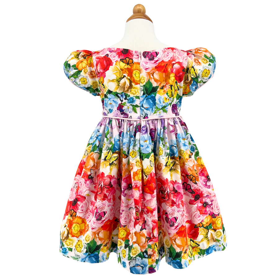 Back view of the Rainbow Bloom Dress on form, showcasing its vibrant floral and butterfly print, puff sleeves, and delicate tie waist