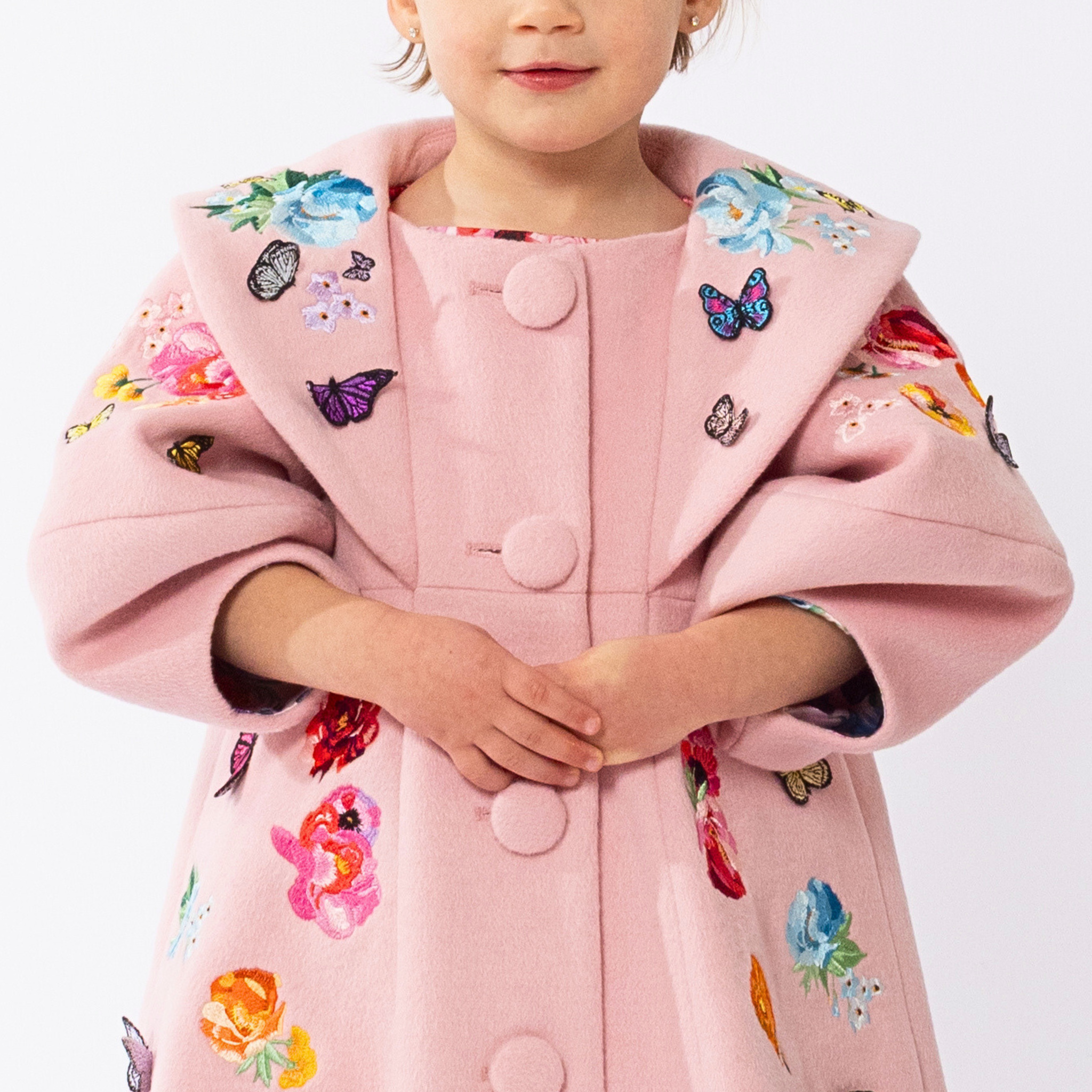 Close-up of pink wool girls' coat with embroidered flowers, butterfly appliqués, and lantern sleeves. Elegant and perfect for special occasions