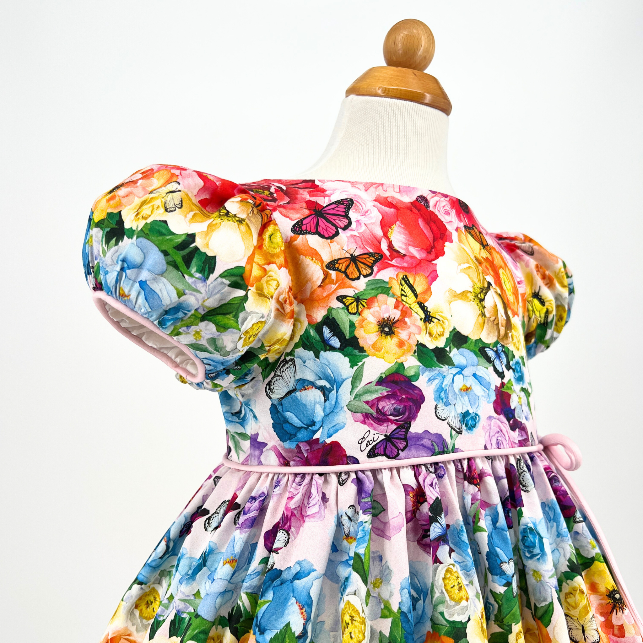 Close-up of Rainbow Bloom Party Dress featuring puff sleeves, pastel floral print, & delicate butterfly details, highlighting fabric texture and design