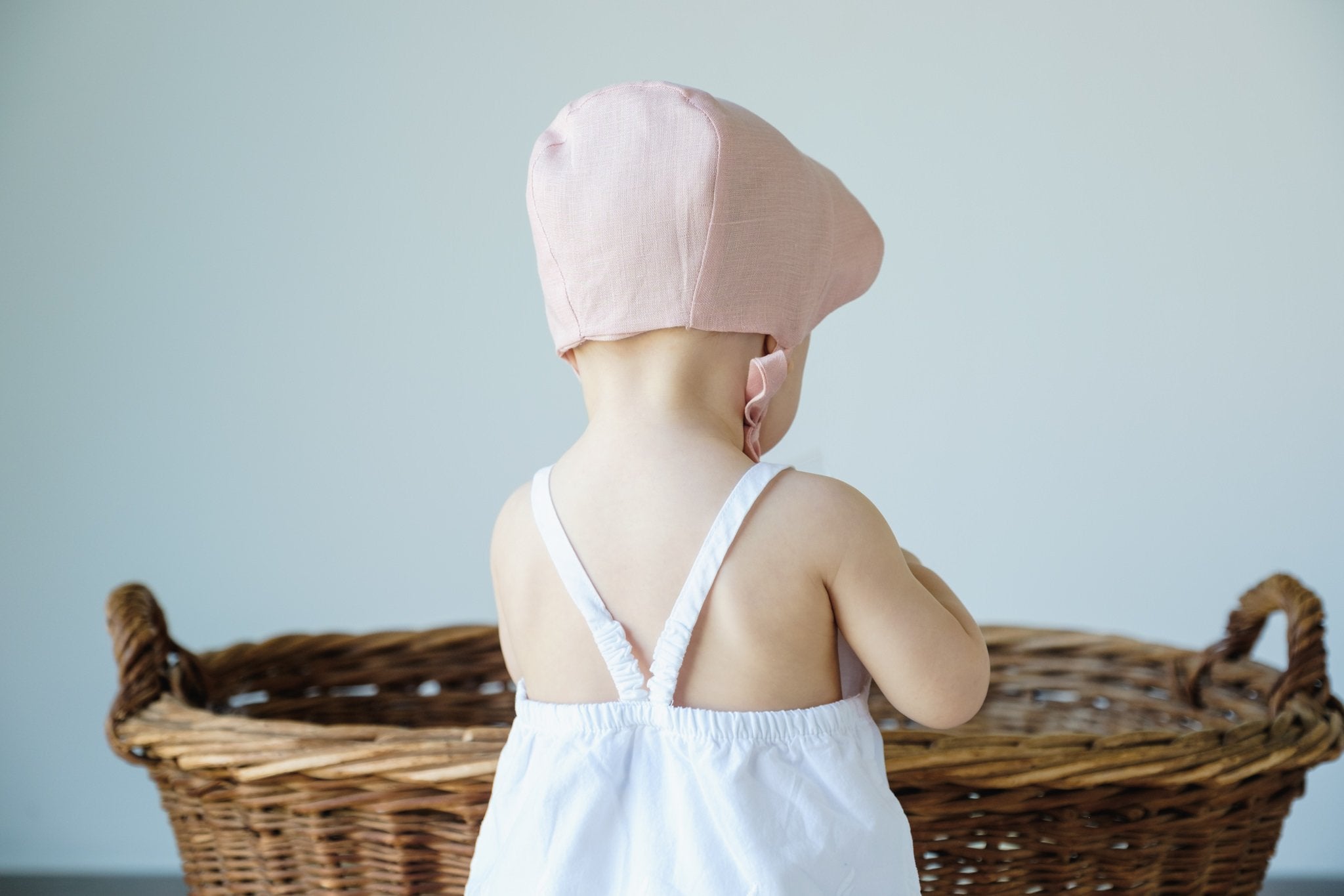 Back view of a baby wearing a shell pink scalloped linen bonnet, showcasing the detailed edging.