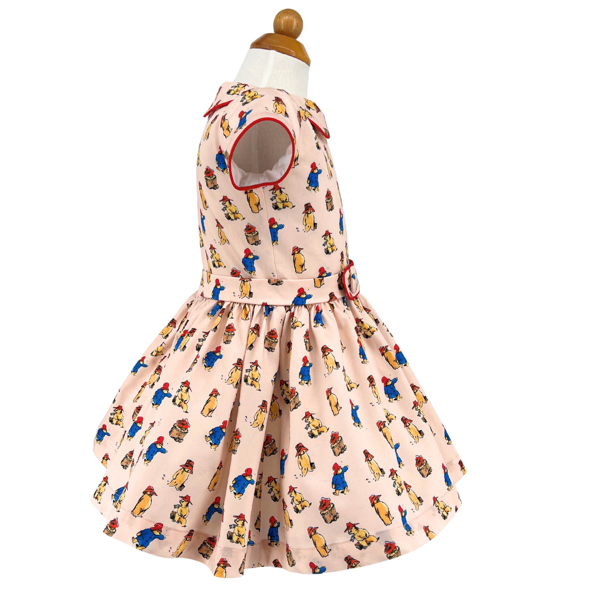 Side view of a vintage-inspired girls' dress with red trim, cap sleeves, belted waist, and full skirt, made from soft printed cotton.