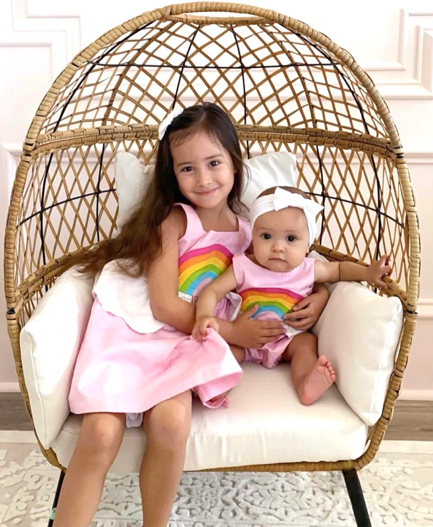 Sisters wearing matching rainbow dress and romper in Sunset Pink with colorful appliques and cloud peplums