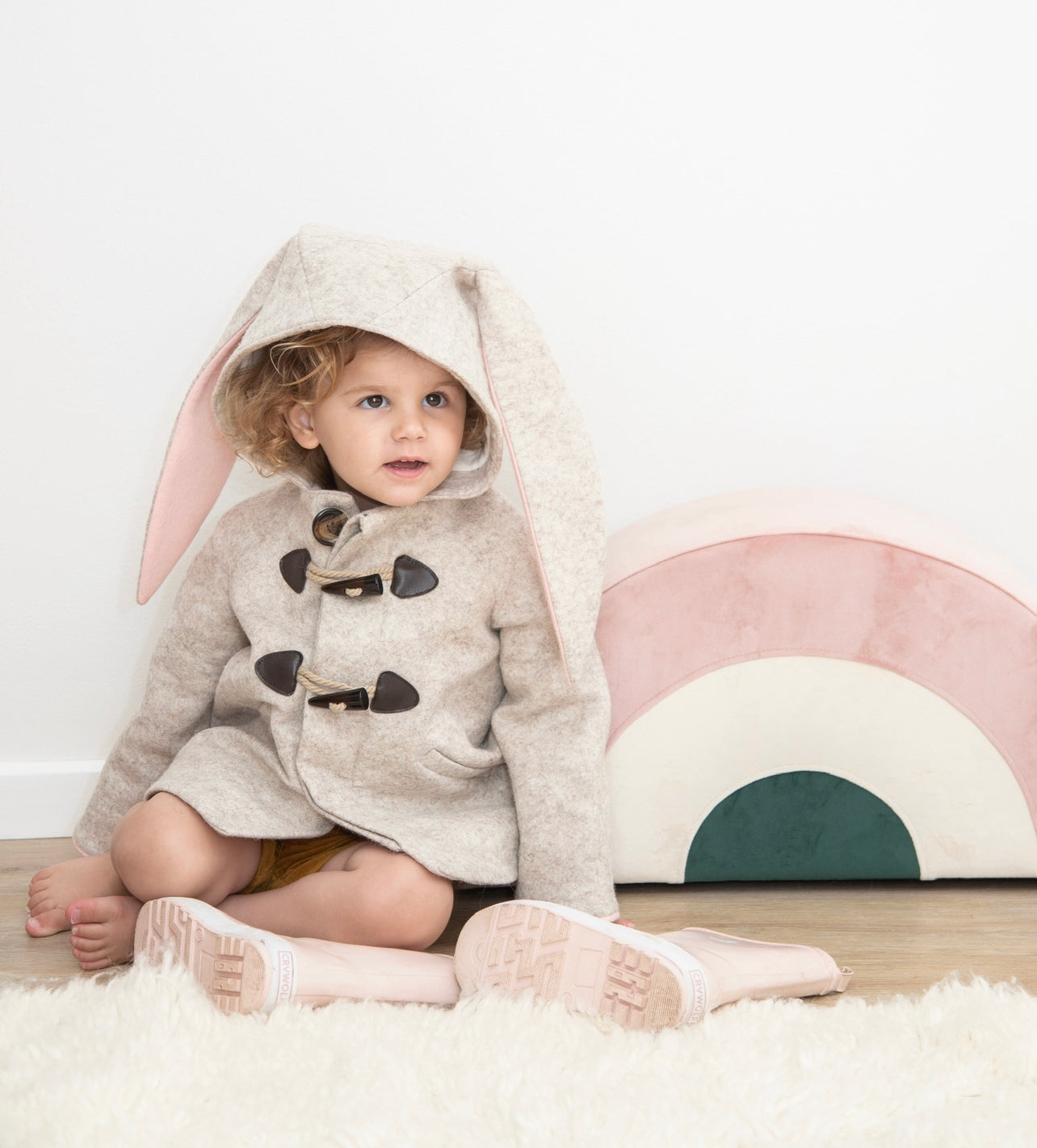 A young girl wearing the Little Goodall Snowshoe Rabbit Coat in merino wool, featuring a bunny ear hood, double-breasted front, and soft faux fur lining.
