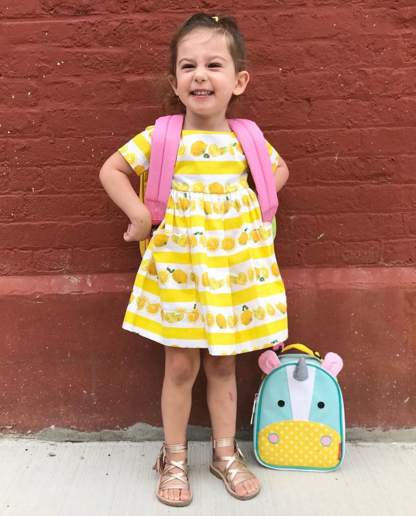 Smiling young girl wearing a lemon print dress with a pink backpack, ready for back to school