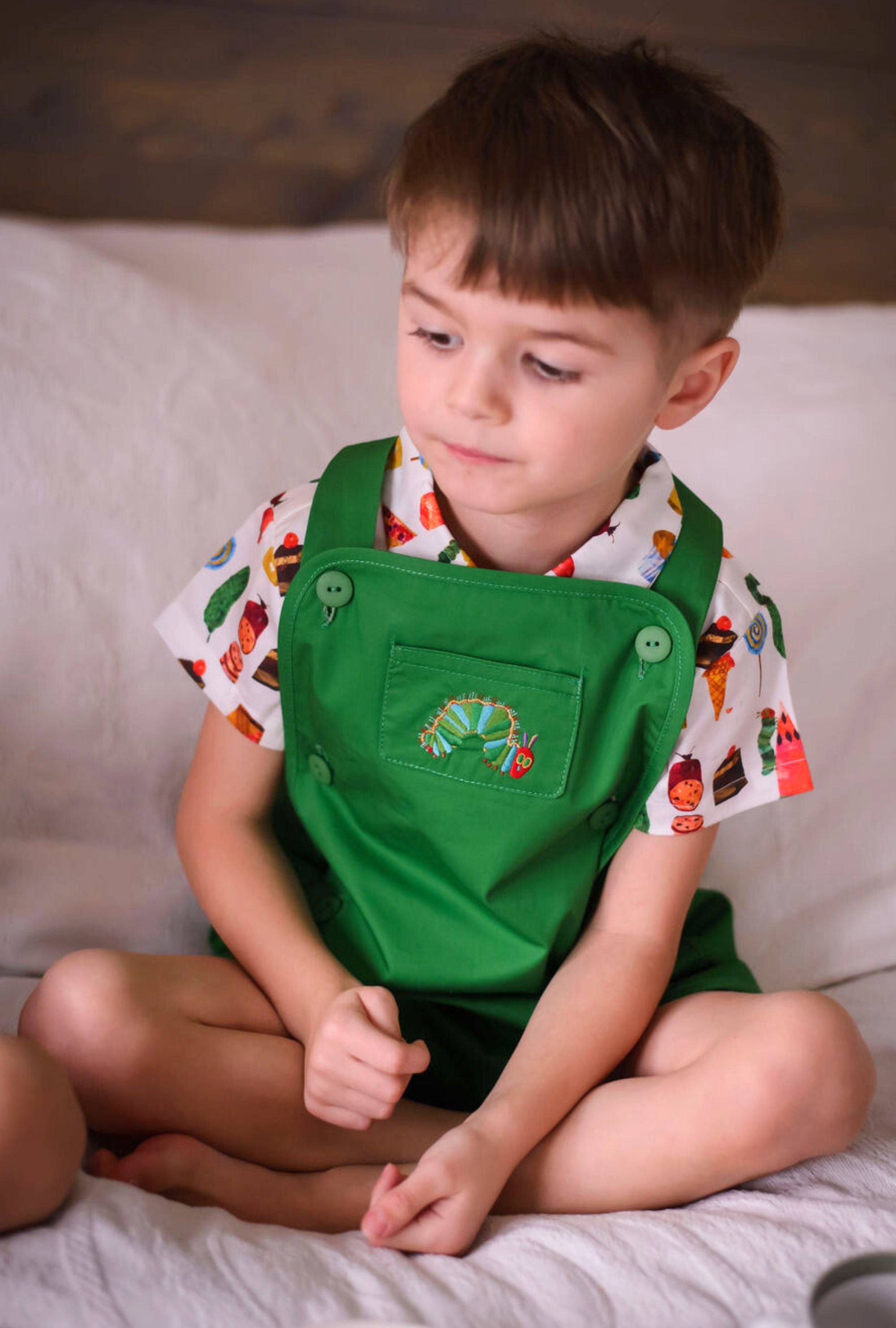 Young boy wearing the Very Hungry Caterpillar romper, featuring green twill fabric, embroidered caterpillar pocket, and colorful food print shirt, 