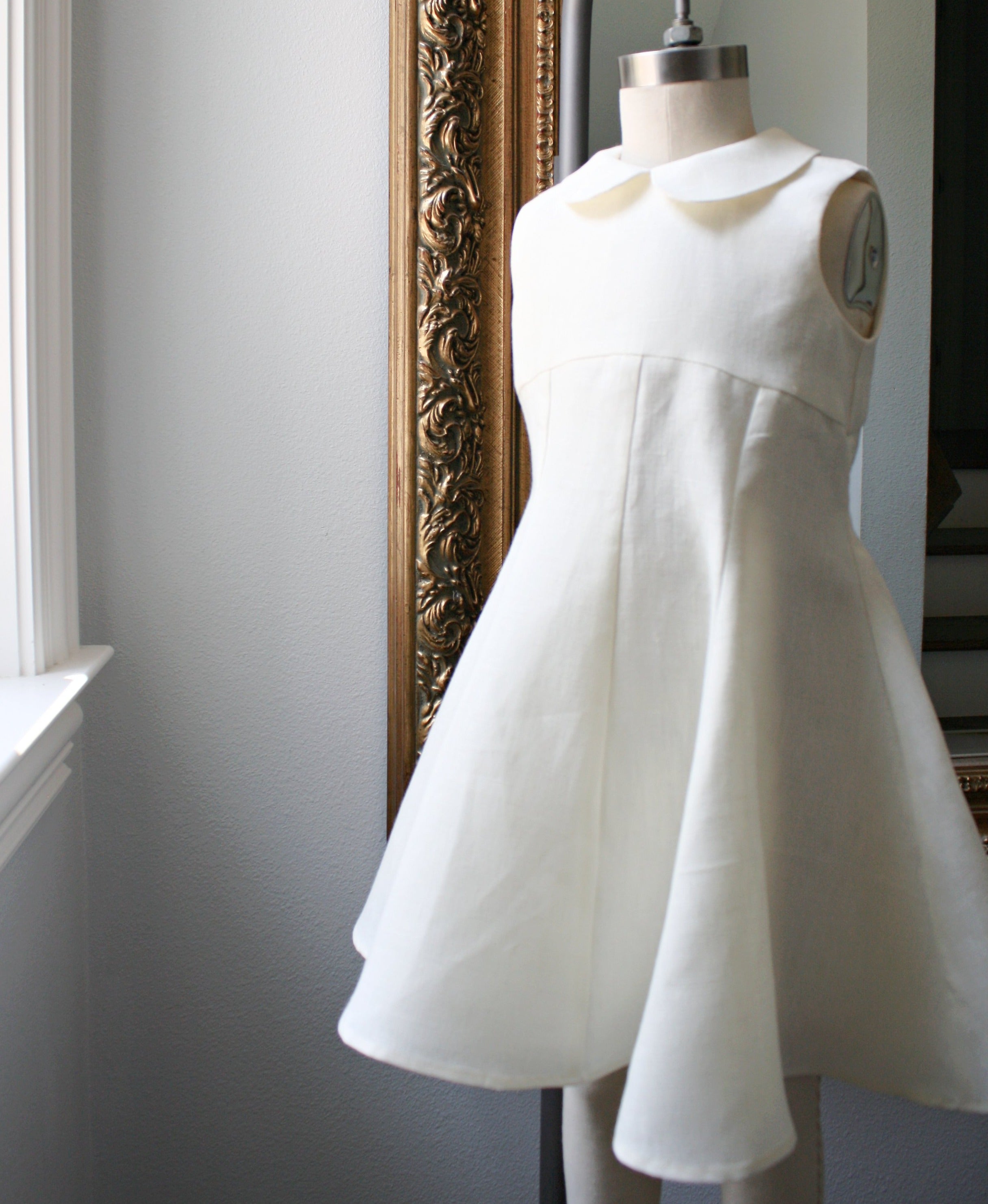 Ivory linen party dress displayed on a mannequin, featuring a Peter Pan collar, empire waist, and flowing princess-seamed skirt